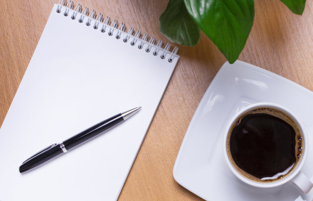 在办公室的木制背景上，有眼镜、一朵绿色的花、一支钢笔、一杯咖啡和一个有空间插入文本的记事本。本空间图片下载