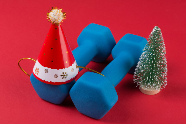 一对蓝色哑铃，一顶圣诞老人帽和一棵圣诞树，红色背景，概念图片下载