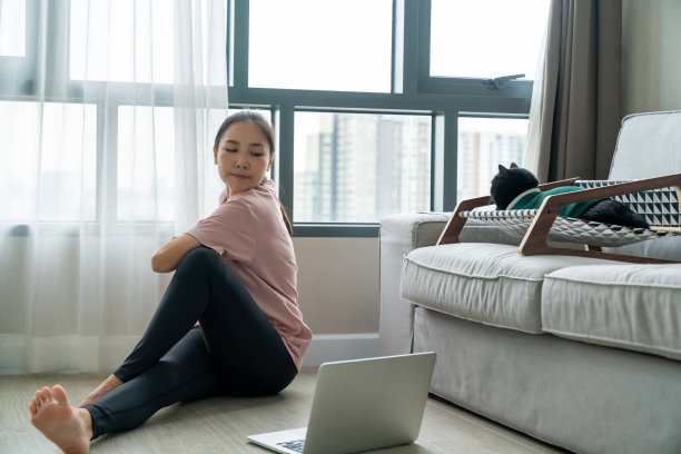 年轻的亚洲妇女通过在客厅的笔记本电脑上观看在线教程来学习锻炼。图片下载