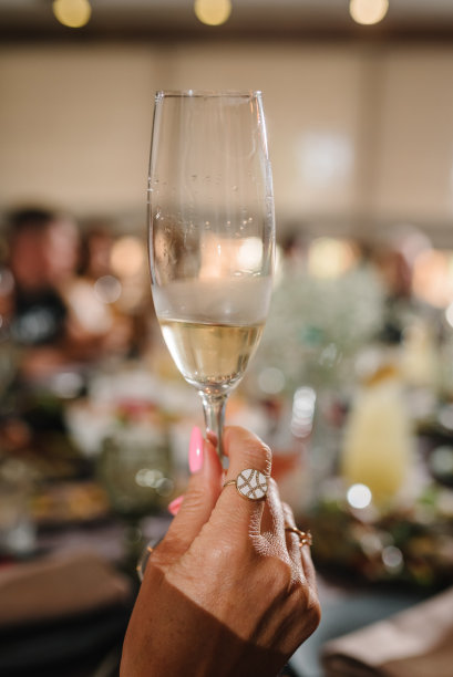 在一群人和朋友的背景下，一个豪华的女人手拿香槟酒杯。女孩庆祝单身派对的特写照片。女性吃土司配酒。图片下载