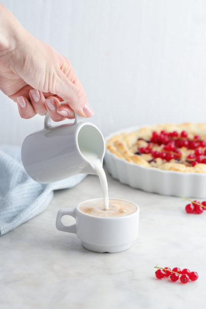 年轻女子把牛奶从壶里倒进咖啡杯里图片下载