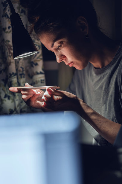 一名妇女在家里的灯光下给自己修指甲。用一次性指甲锉处理指甲，抛光和塑形图片下载