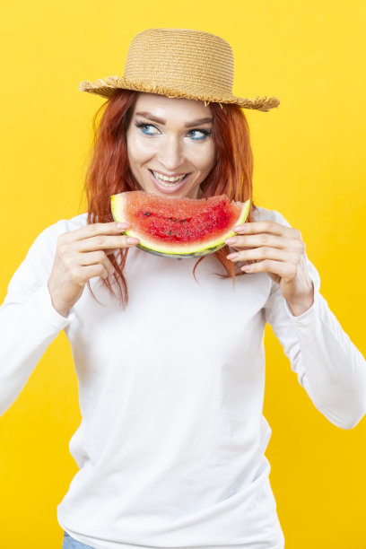 一个迷人的白人漂亮的年轻女子在草帽与多汁西瓜的彩色背景。图片下载