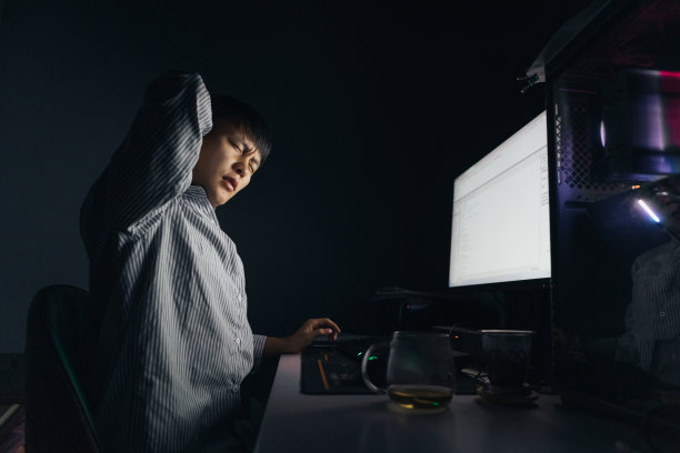一名亚洲男子晚上在电脑前加班，感到脖子和脖子疼痛——这是不健康的生活方式图片下载