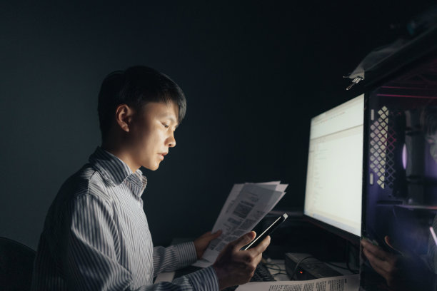 一名亚洲男子晚上在电脑前加班，仔细检查数据——不健康的生活方式图片下载