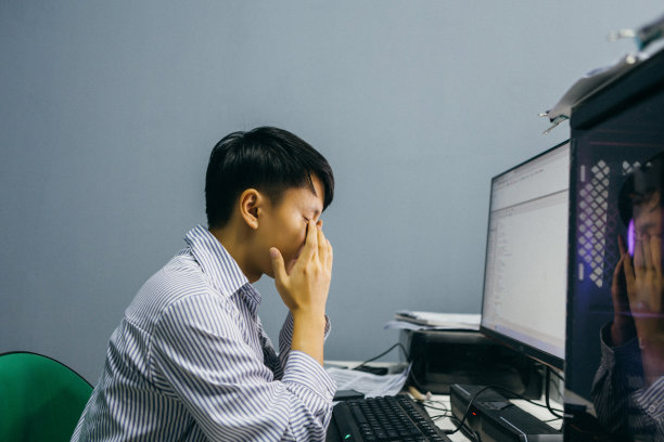 一名亚洲男子晚上在电脑前加班，感到眼睛很累——这是一种不健康的生活方式图片下载