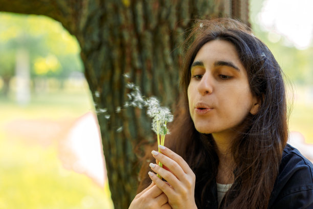 女孩在夏日阳光明媚的日子里吹着白色的蒲公英。图片下载