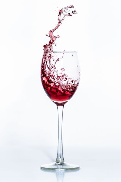 在白色背景下，垂直拍摄玻璃杯中红酒的飞溅图片下载