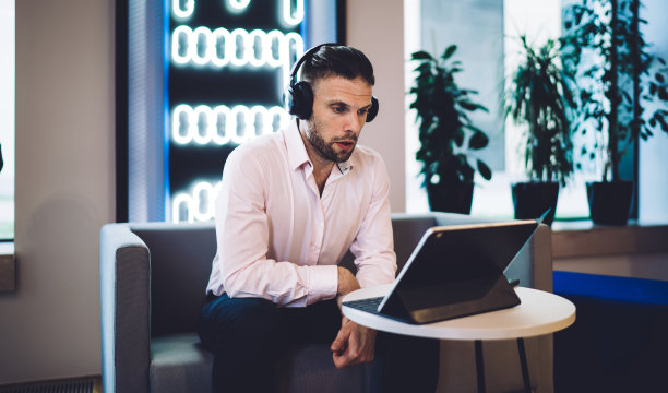 商人戴着耳机坐在沙发上使用平板电脑图片下载