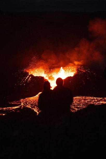 垂直拍摄的一对夫妇的剪影观看熔岩从冰岛的一座火山在夜间流出图片下载