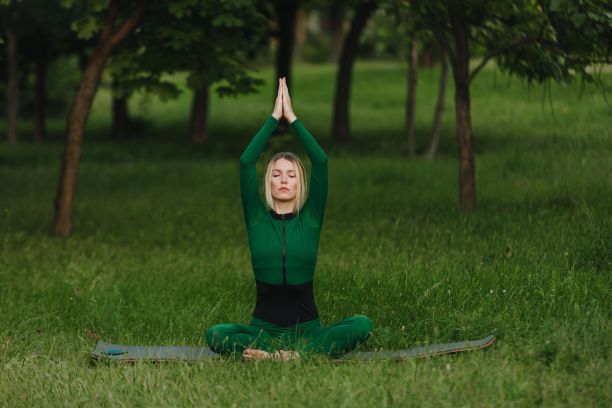 早上在公园的绿色草地上练习瑜伽体式的年轻女性图片下载