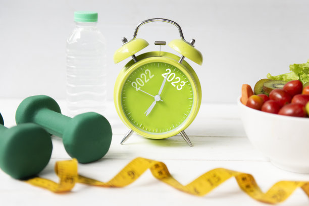2022年和2023年的闹钟上有节食的锻炼计划。运动锻炼器材健身和健身房营养新鲜沙拉的健身。圣诞快乐和新年快乐的概念图片下载