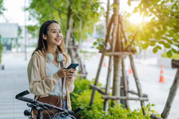 美丽的亚洲女人听喜欢的音乐耳机从手机，快乐放松夏天在公园与音乐骑自行车在绿色公园。图片下载