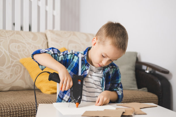 男孩用热熔胶枪用纸板制作自己的工艺品。支持创意手工制作，让孩子在家享受创意休闲。图片下载