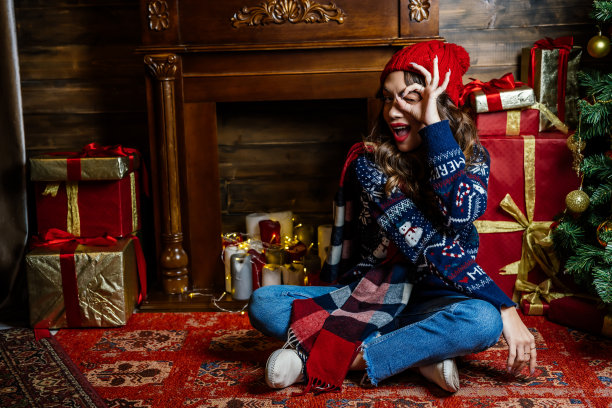 一位美丽的黑发女子坐在圣诞树下，背景是新年的装饰。图片下载