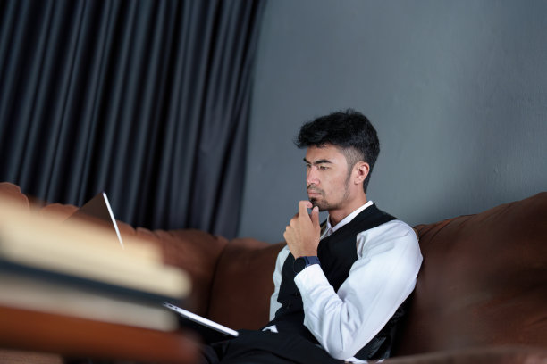 画像一个英俊，谨慎的亚洲人坐在沙发上使用电脑图片下载