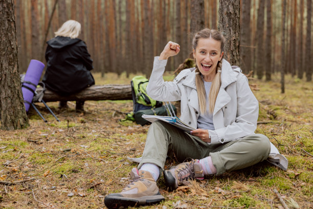 妈妈和女儿在树林里徒步，在前景年轻的女人是快乐的结束了家庭作业，抱着书在手臂微笑的背景老妇人坐在相机后面图片下载