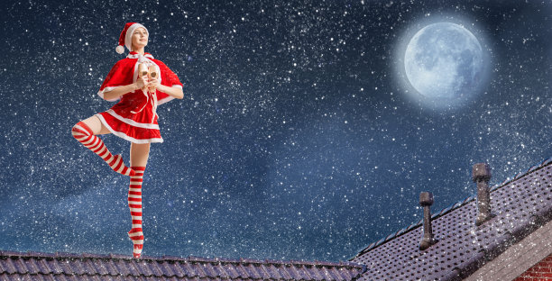 圣诞夜，在满天繁星的背景下，身穿圣诞老人服装、手拿礼物的芭蕾舞女演员站在屋顶上。图片下载