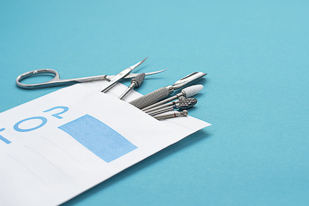 一套装在纸袋上的金属美甲剪刀和剪刀，用于杀菌。在蓝绿色背景上的布局。图片下载