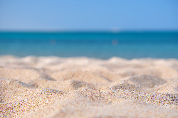 特写干净的黄沙表面覆盖的海滩与蓝色的海水为背景。旅游和假期的概念。图片下载