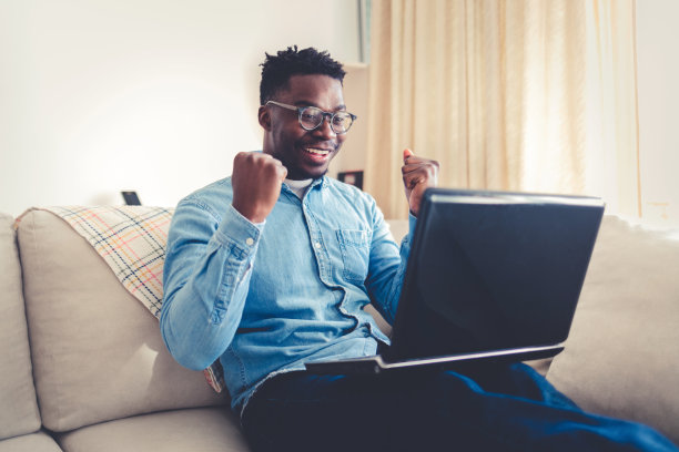 快乐的年轻商人在家里使用笔记本电脑。年轻人在家里用电脑工作。随意的企业家在家里用笔记本电脑工作时对新项目感到兴奋。图片下载