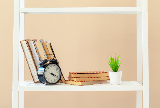 白色的书架上有书和文具，靠着米色的墙图片下载