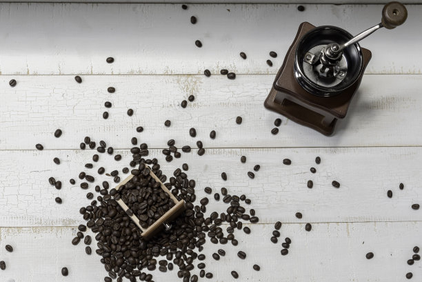 咖啡的咖啡豆铺在白色的木头上，靠近手磨咖啡准备研磨和酿造。图片下载