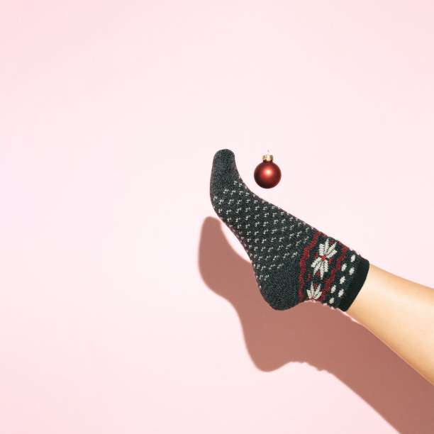 女人的腿在圣诞袜踢红色装饰节日小玩意在粉红色的背景。图片下载