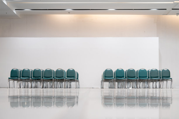 一间宽敞的大厅里有许多空的绿色皮椅子，灯还亮着。地板反射物体。给人一种空虚的感觉。图片下载