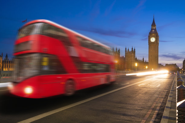 伦敦大本钟和威斯敏斯特桥上的议会大厦，红色巴士在夕阳下闪烁图片下载