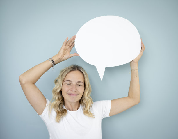 漂亮的金发卷发的年轻女子站在蓝色的墙前，拿着演讲泡沫图片下载