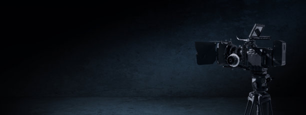 黑暗中的数码电影摄影机。摄像机架在三脚架上，在一个有光和影的黑色反墙房间里。电视纪录片或电影制作横幅背景与复制空间图片下载