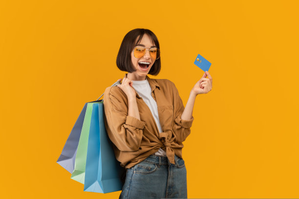 简单的购物理念。兴奋的女人拿着信用卡和购物袋，张大嘴巴看着相机图片下载