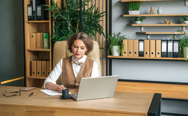 自信，时尚，成熟，中年，老年女性在职。使用笔记本电脑办公，使用手机通话。总经理、首席执行官。年长的高级女商人，60年代西装革履的女士，高级商业领袖。企业家的事业。会计在银行图片下载