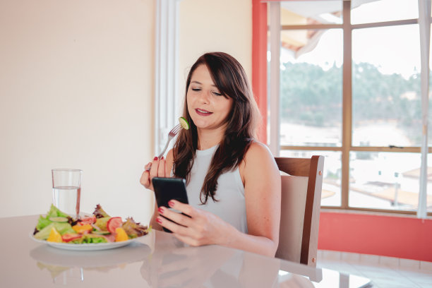 女性在家吃健康食品，使用智能手机图片下载