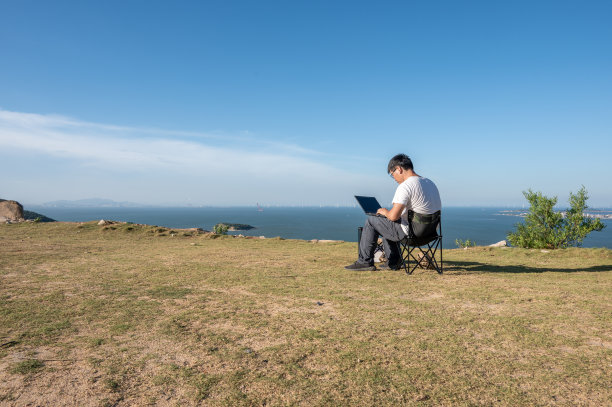 在野外的海边，一个亚洲人在简单的桌椅上使用电脑图片下载