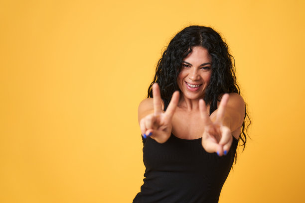 一个年轻女孩的肖像与胜利的姿态和一个大大的微笑在黄色的背景图片下载