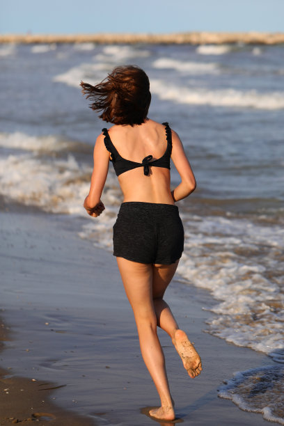 在日出锻炼期间，赤脚女孩在前海岸的海滩上跑步图片下载