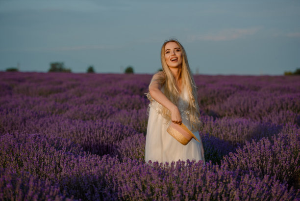 年轻漂亮的女人穿着白裙子，戴着帽子，走在薰衣草田里。图片下载