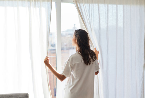 清晨，年轻女子从自家窗户向外望去。图片下载