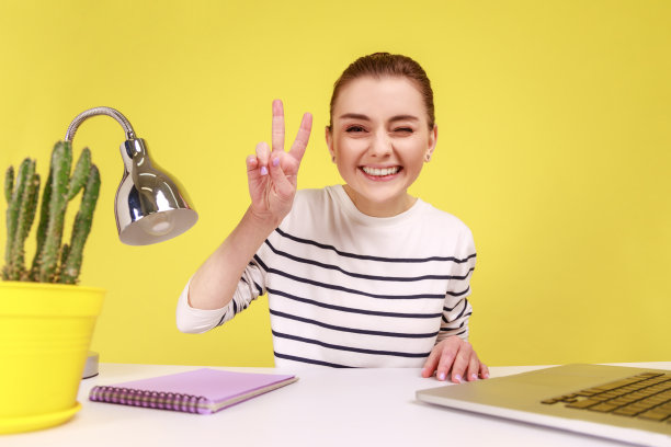 坐在工作场所的妇女，看着相机的视角，照片的视角，展示着胜利的姿态。图片下载