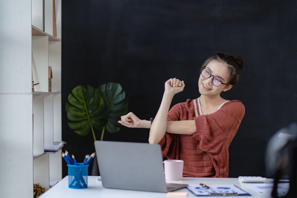 一名亚洲妇女在使用笔记本电脑和概念金融图形办公室综合症时伸展手臂放松图片下载