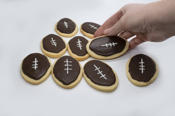足球形状的饼干。手拿饼干。自制饼干的概念。超级碗派对饼干。图片下载