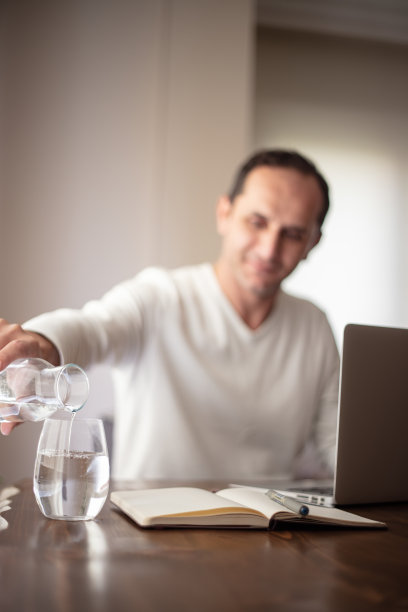 一个人在家里工作，把他的杯子装满水。图片下载