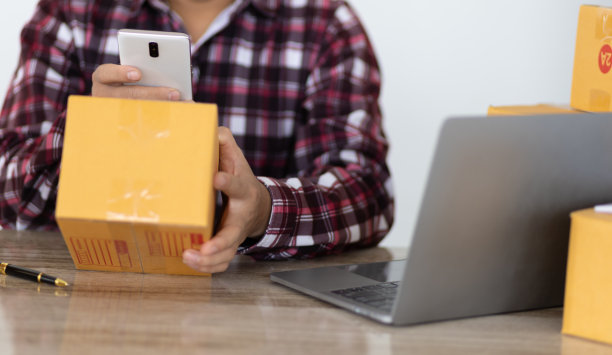 小企业主使用智能手机上的移动应用程序扫描条形码检查包裹盒子。一个在网上经营小生意的人用手机拍下了寄给顾客的包裹。图片下载
