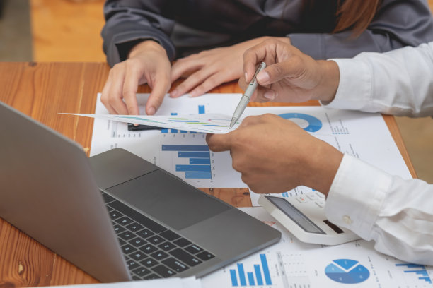 两名男性和女性营销人员使用公司文件和笔记本电脑记录数据，分析公司利润。图片下载