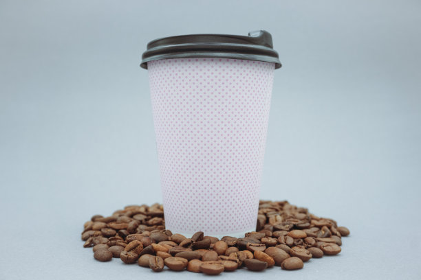 粉色纸杯和塑料盖模型或模型，灰色背景。分散的咖啡豆。图片下载
