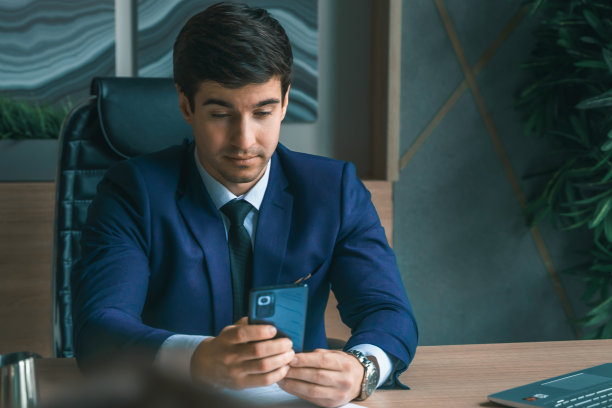 西装革履的商人手里拿着手机。男人打字留言，使用社交网络。检查消息。商务会议。现代办公室。总经理、首席执行官。打电话来的合作伙伴。计划工作时间图片下载