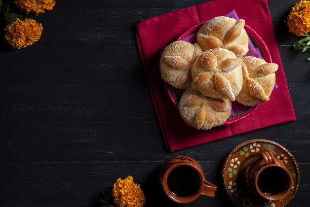 传统的墨西哥死者面包也被称为“Pan de Muerto”在传统的墨西哥餐具上，橙色的花被称为cempasuchil在木制背景上。图片下载