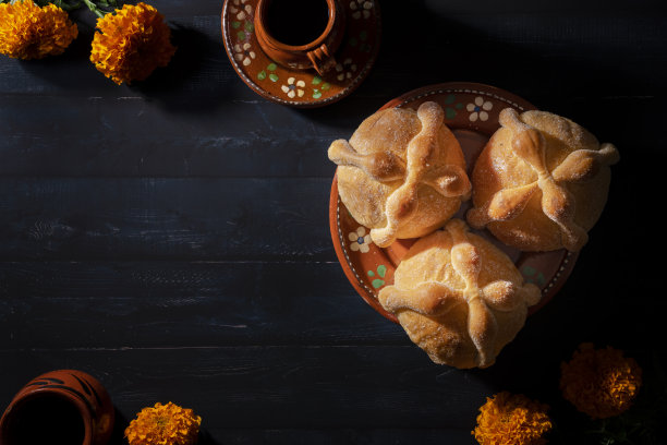 传统的墨西哥死者面包也被称为“Pan de Muerto”在传统的墨西哥餐具上，橙色的花被称为cempasuchil在木制背景上。图片下载